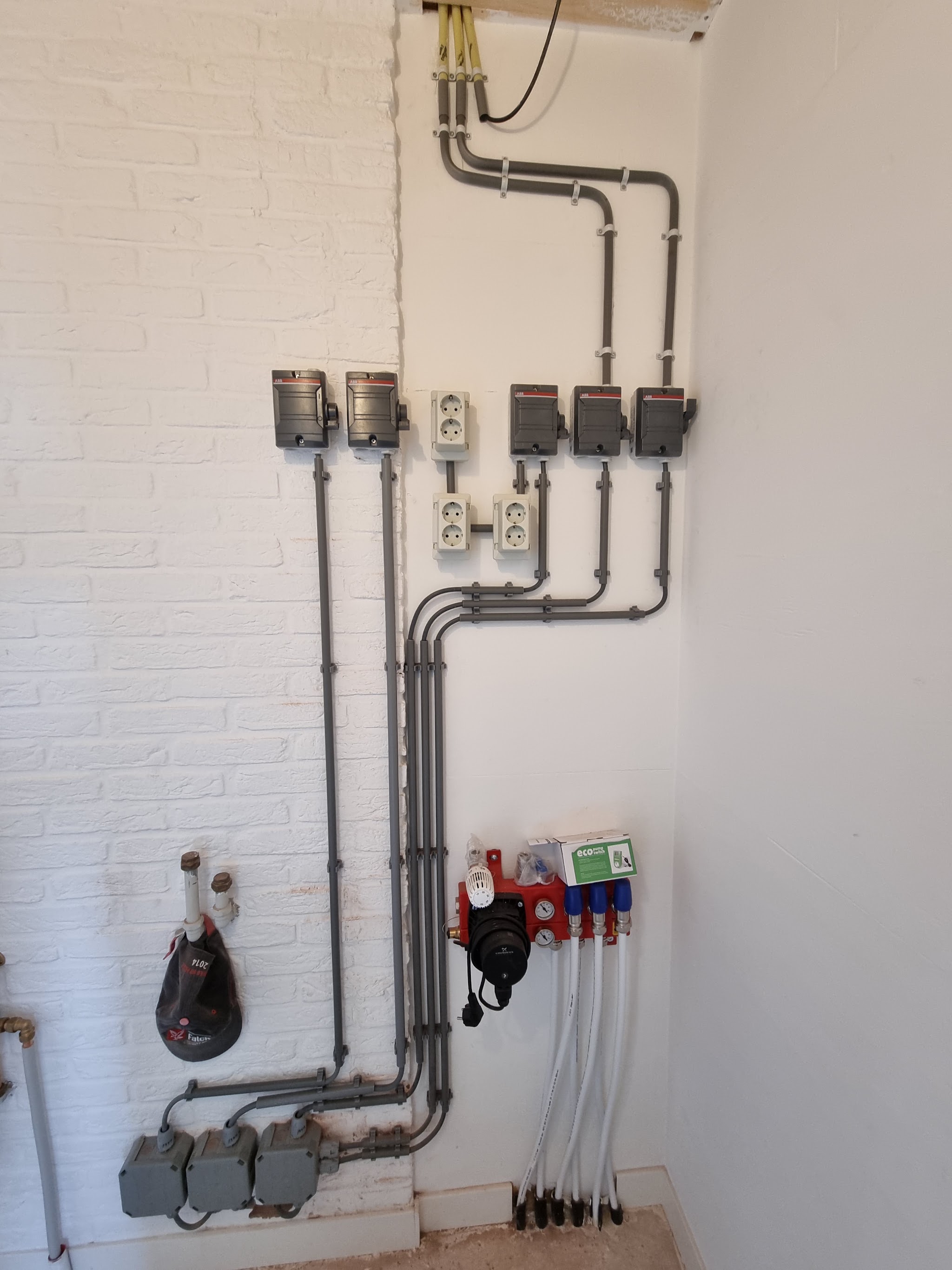 Opbouw leidingwerk met wandcontactdozen en waterleidingen tegen een witte bakstenen muur