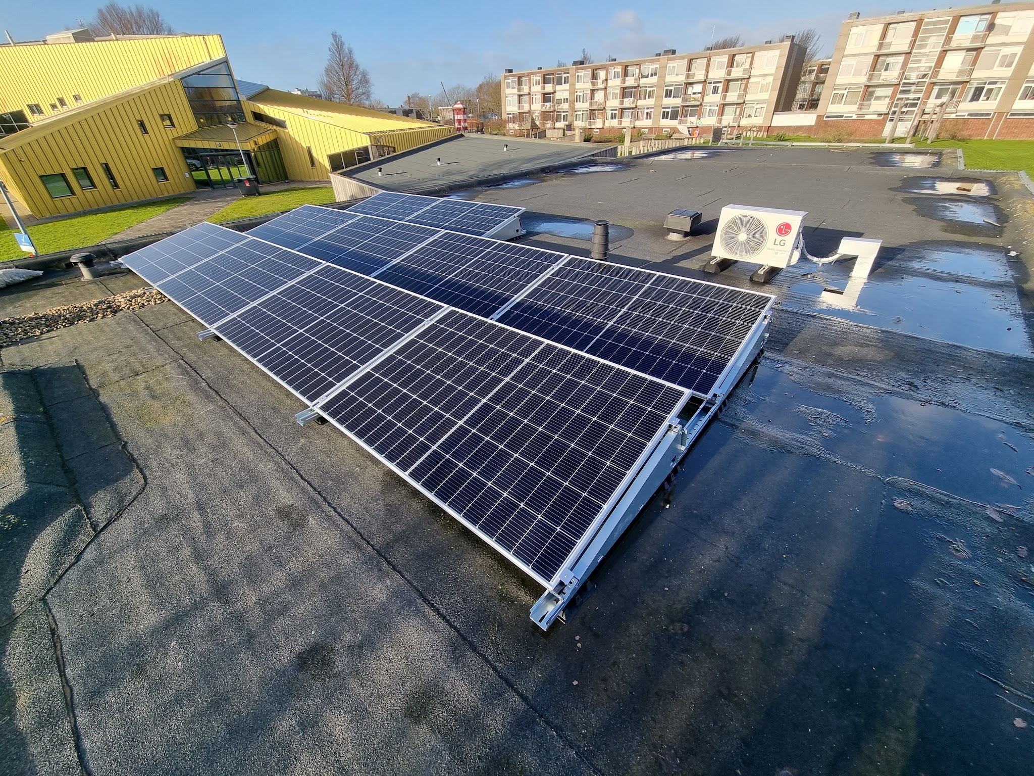 Rij zonnepanelen op een plat dak onder een blauwe lucht