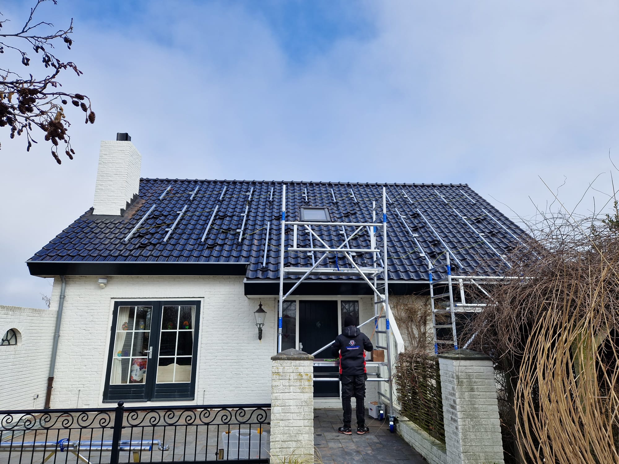 Wit huis met zwart pannendak en een rolsteiger aan de voorkant, met een vakman op de steiger